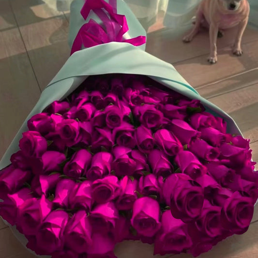 Large bouquet of pink roses with a dog sitting nearby on a wooden floor.