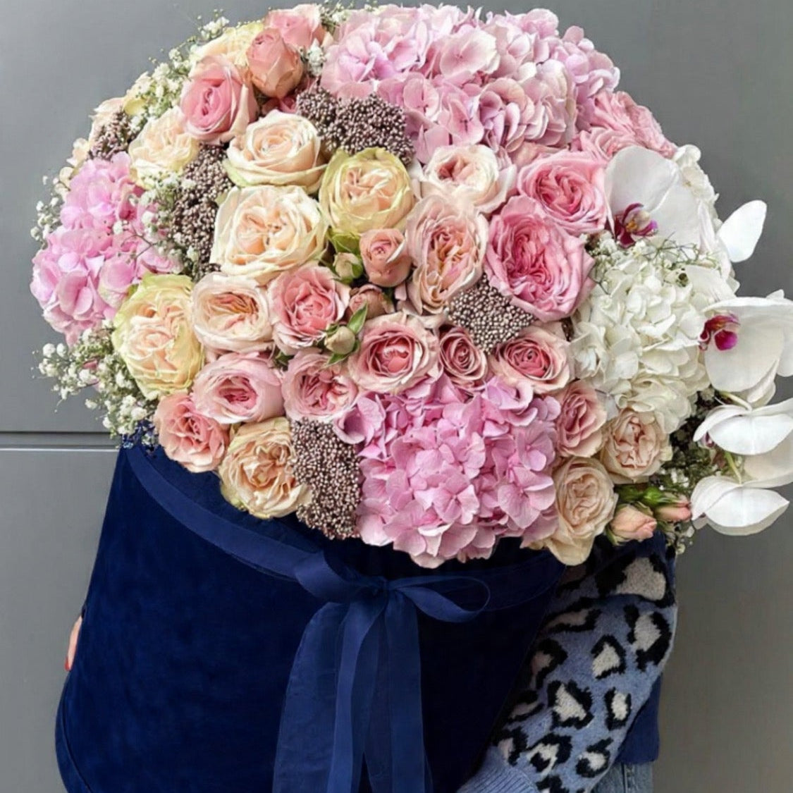Bouquet of pink, white, and yellow flowers with a blue ribbon held by a person.