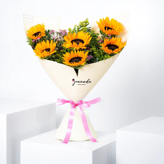 Bouquet of sunflowers wrapped in white paper with a pink ribbon on a white background