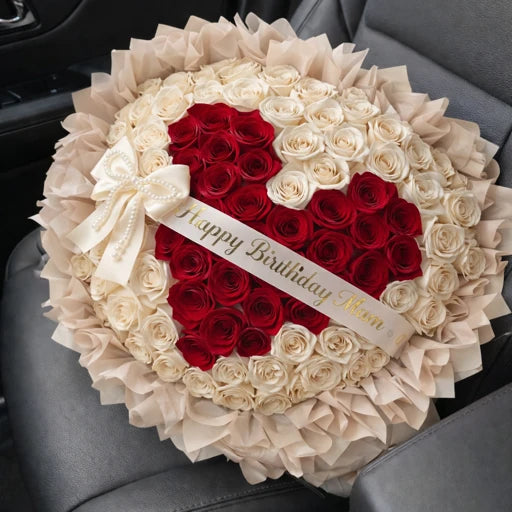 Heart-shaped arrangement of red and white roses with a 'Happy Birthday Mom' card on a car seat.