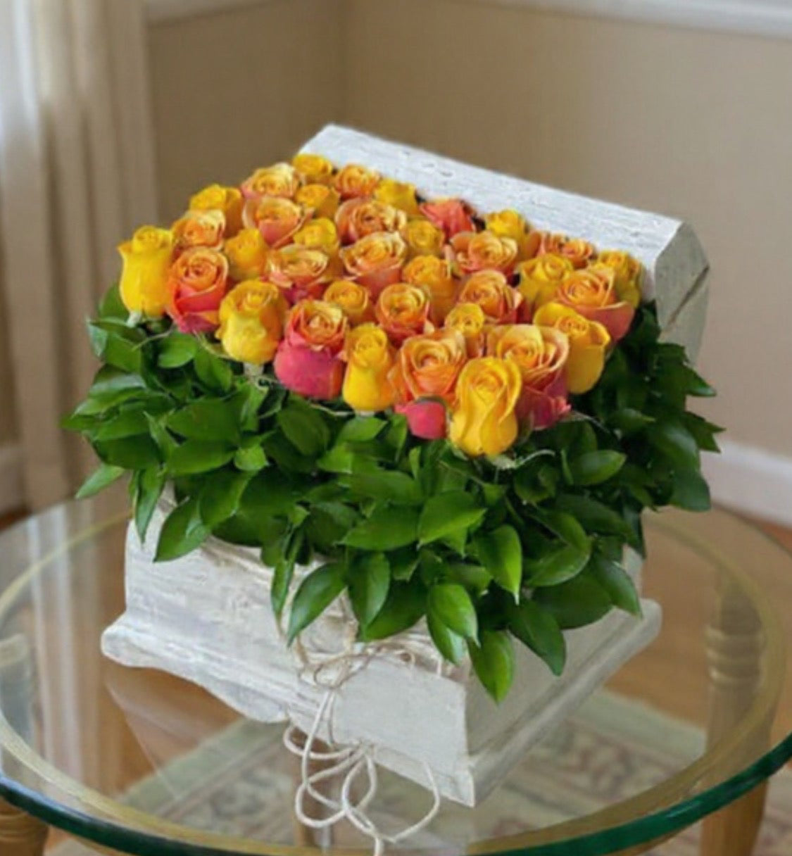 Box of yellow and pink roses on a glass table