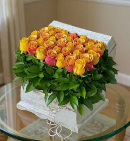 Box of yellow and pink roses on a glass table