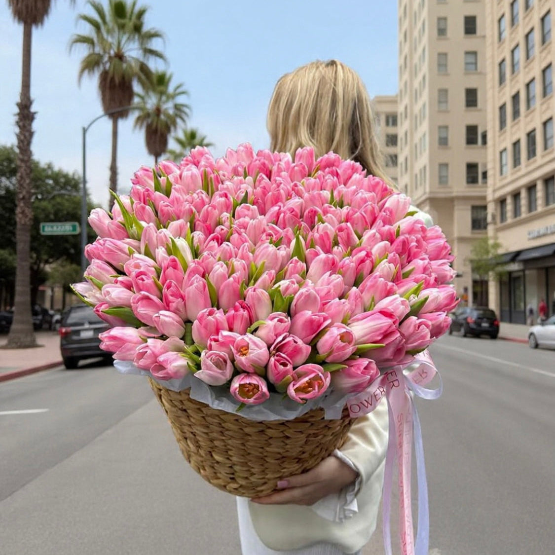 Person holding a large bouquet of pink flowers on a city street.