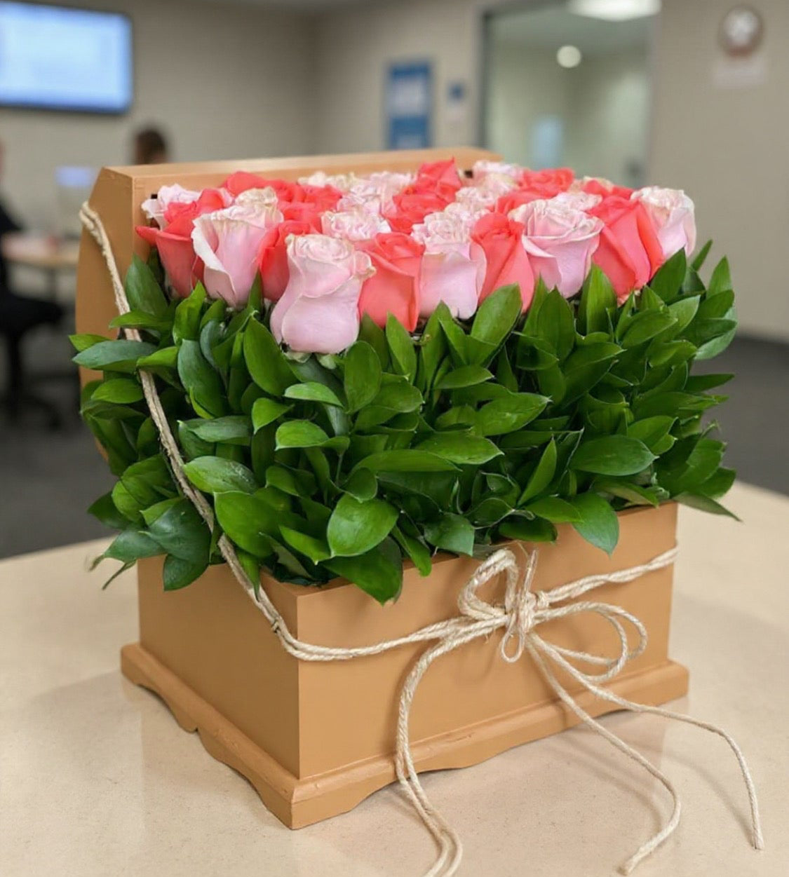 Box of pink and white roses with green leaves on a blurred office background