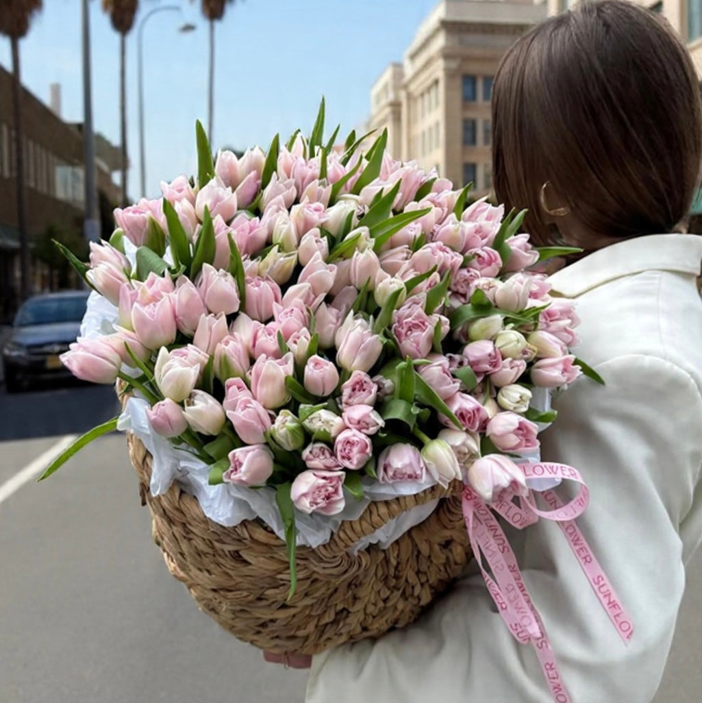 Person holding a large bouquet of pink tulips on a city street.