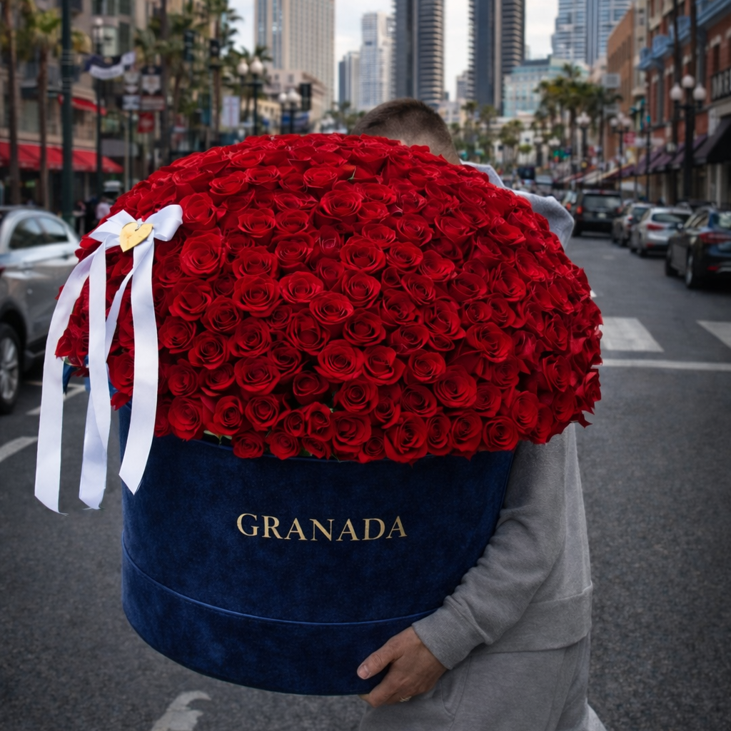 Person carrying a large bouquet of red roses in a blue box labeled 'Granada' on a city street.