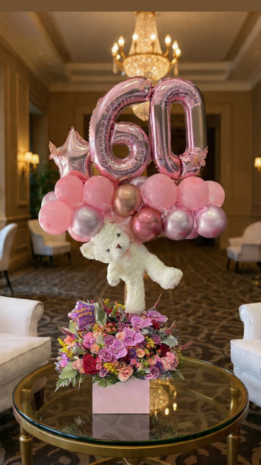 Decorative setup with balloons, flowers, and a teddy bear on a table in an elegant room.