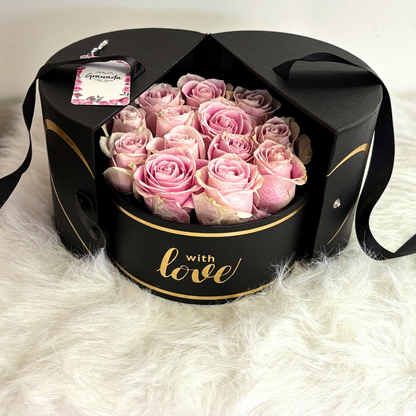 Luxurious black round floral box with "With Love" in gold lettering, filled with soft pink roses, elegantly arranged by Granada Floral.