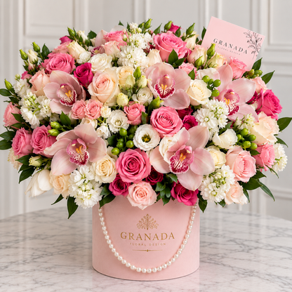 Pink and cream roses with pink orchids and white flowers in a blush Granada Floral Design box with a pearl-style handle